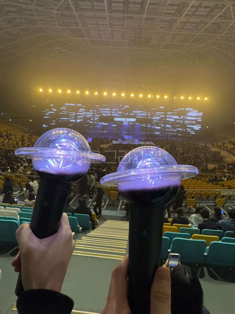 체조경기장 내부에서 무대를 배경으로 홀봉 두 개를 함께 들고 있다.