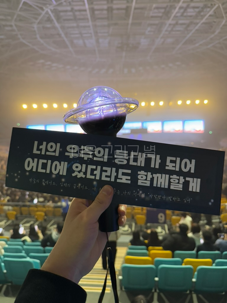 체조경기장 내부에서 무대를 배경으로 홀봉과 슬로건을 들고 있다. 슬로건에는 '너의 우주의 등대가 되어 어디에 있더라도 함께할게' 문구가 적혀있다.