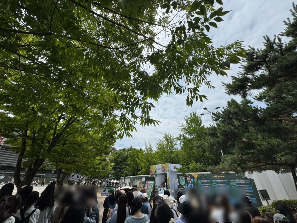 사람들이 자신의 번호에 맞춰 줄을 서있다. 번호 범위를 알려주는 팻말이 놓여있고, 뒤로는 우측에 우선입장권 전용 입장 게이트가 보인다. 벽에는 타임테이블이 붙어있다.