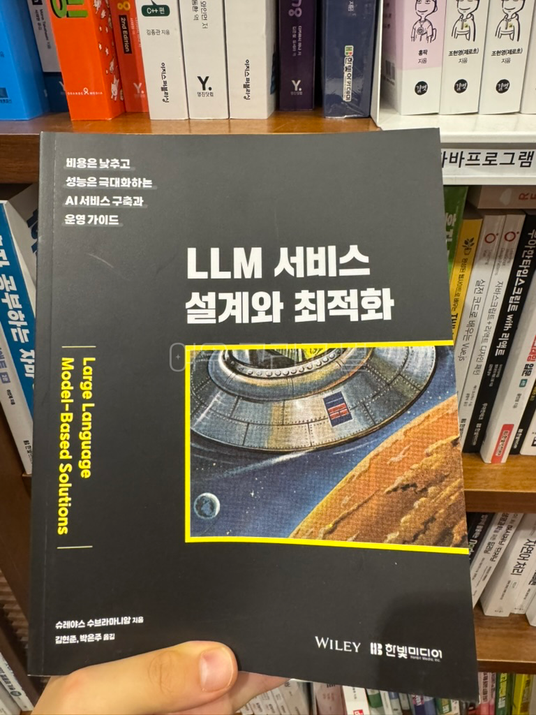 책장을 배경으로 검은색 배경의 'LLM 서비스 설계와 최적화' 책을 들고있다.
