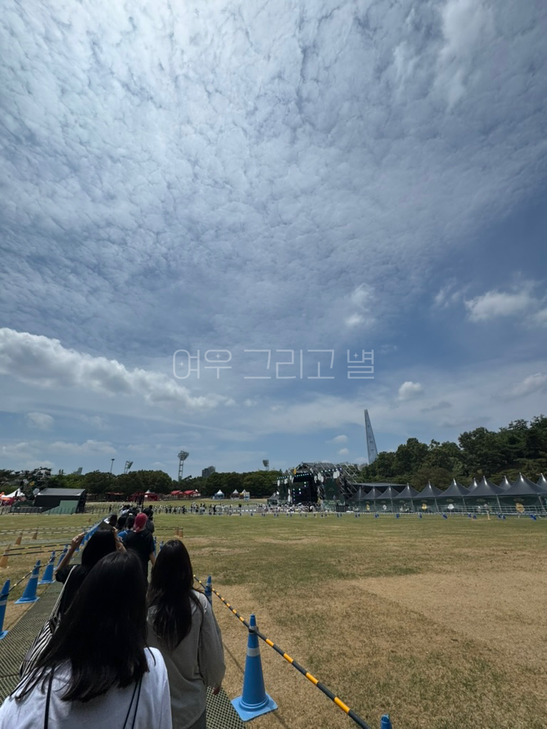 잔디마당 한가운데에서 입장하는 행렬을 촬영한 장면이다. 스탠딩존과 피크닉존이 보이며 무대와 여러 부스가 보인다.