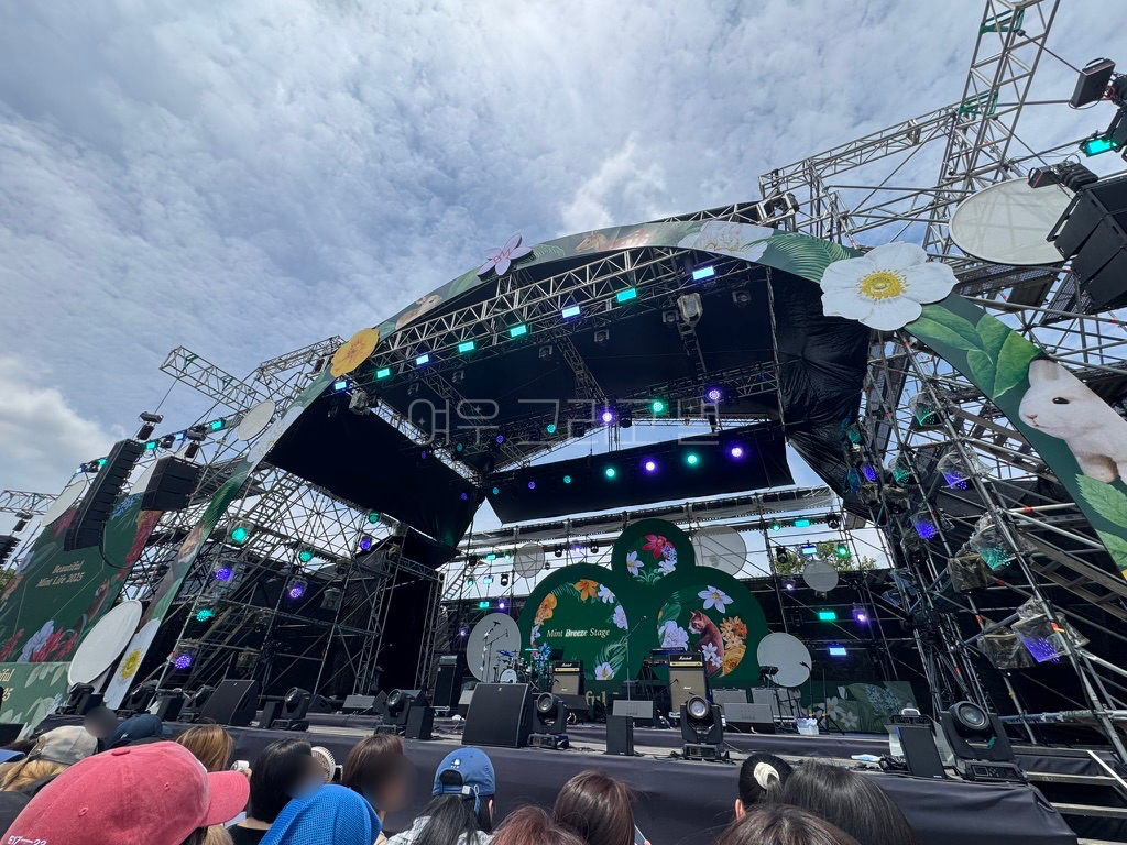 스탠딩존에서 무대를 광각으로 촬영한 장면이다. 토끼와 고양이, 꽃을 표현한 그림들이 반원 형태로 무대 앞 부분을 꾸미고 있다. 세개의 원이 합쳐진 형태의 무대 뒤 전광판에는 토끼와 고양이, 꽃을 표현한 그림이 송출되고 있다. 무대 위에는 여러 악기와 장비들이 세팅되어 있다.